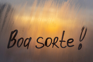 Lettering Spanish text Boa sorte Good luck in english message written finger on foggy glass wet sunset window
