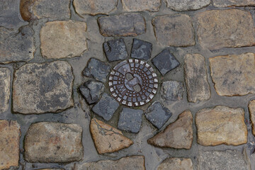 Old metal sewer hatch in the middle of the road, laid out of a smooth paving stone