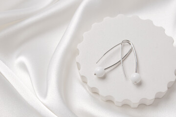 Two silver earrings with white agate on a concrete podium on silk. Beautiful accessories for women....