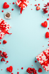 Valentine's Day concept. Top view vertical photo of gift boxes with ribbon bows heart shaped chocolate candies candles and sprinkles on isolated pastel blue background with copyspace in the middle
