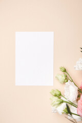 Obraz na płótnie Canvas Holiday greeting card mockup with flowers on light beige background, top view, flat lay. White wedding invitation card mockup and floral decor