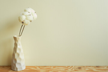 Vase of soft cotton branch on wooden table. ivory wall background. home interior, minimal, copy space
