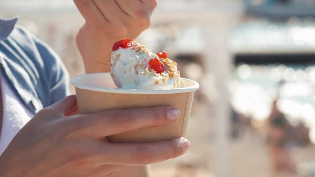 Close-up of a girl on the beach eating a newlywed. A woman eats yogurt ice cream with cherries and peanuts. a woman's hand takes ice cream with a spoon