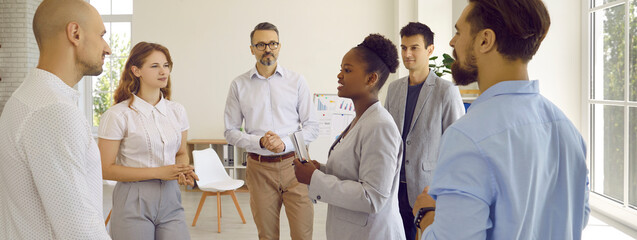 Woman manager gives assignments to her employees during meeting before start of working day. Men...