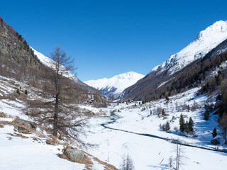 Fototapeta na wymiar Val d'Arolla, Switzerland - April 10th 2022: A small stream meandering through a snow covered plain