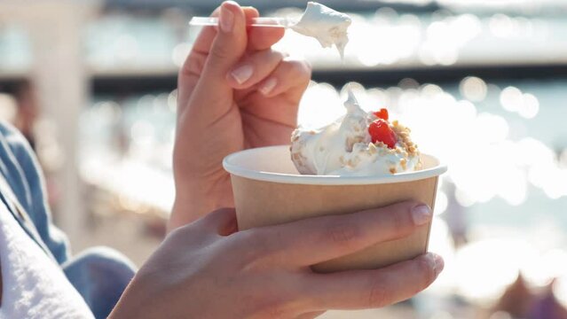 Close-up of a girl on the beach eating a newlywed. A woman eats yogurt ice cream with cherries and peanuts. a woman's hand takes ice cream with a spoon