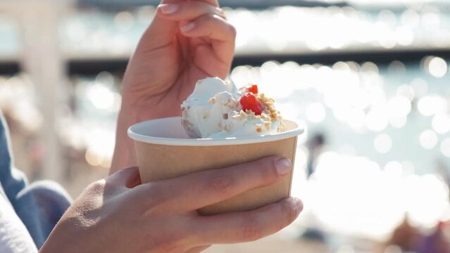 Close-up of a girl on the beach eating a newlywed. A woman eats yogurt ice cream with cherries and peanuts. a woman's hand takes ice cream with a spoon