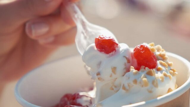 Close-up of a girl on the beach eating a newlywed. A woman eats yogurt ice cream with cherries and peanuts. a woman's hand takes ice cream with a spoon