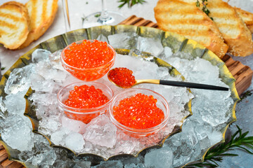 Red caviar in glass bowls on a metal tray with ice. On concrete texture background. Top view.