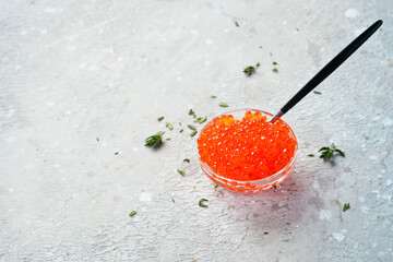 Red caviar in a glass bowl. Macro photo. On a gray concrete background. Side view.