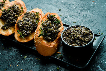 Toasts with black caviar on a stone plate, caviar in a bowl. On a black stone background. Rustic...