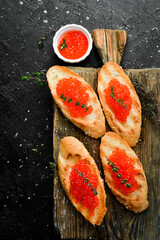 Red caviar and sandwiches with caviar on a wooden board. On a black stone background. top view
