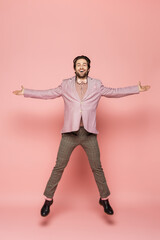 Positive and stylish host of event looking at camera while jumping on pink background