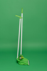 broom and plastic scoop on green background, housekeeping concept
