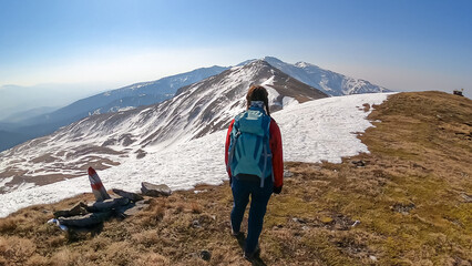 Fototapeta premium Rear view of woman with backpack looking at snow capped mountain peak Zirbitzkogel and Kreiskogel, Seetal Alps, Styria (Steiermark), Austria, Europe. Hiking trail Central Alps in sunny early spring