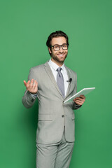 cheerful journalist in eyeglasses and suit holding digital tablet on green