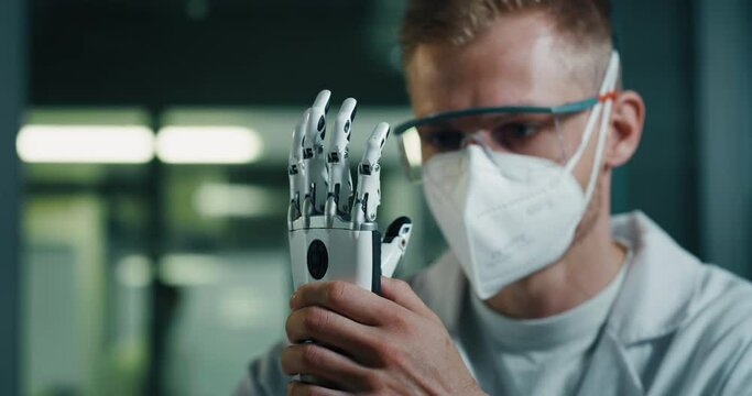 Close Up of Young Engineer Adjusting Modern Bionic Limb With A Screwdriver. Man Wearing Protective Face Mask And Glasses While Working On Advanced Robotic Palm For Person With Disability.