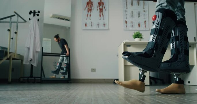 Young Biomedical Engineer Is Testing New Bionic Limb Prosthesis For Client With Disability. Man Is Wearing Adapters to Assess Functionality of Artificial Feet. Using Rehabilitation Parallel Bars.