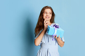 Portrait of young girl in cute tender dress posing over blue background. Birthday celebration. Gifts, presents