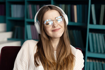 A smart female student with glasses listens to audiobook podcast music during a break.