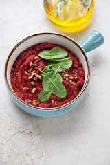 Beetroot caviar with spinach leaves and pine nuts in a turquoise serving bowl, vertical shot on a beige stone background