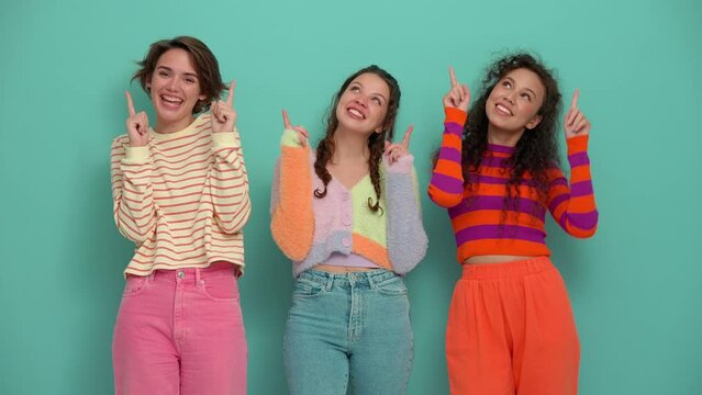 Three smiling young girls pointing fingers at the camera and up in the turquoise studio