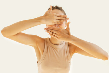Cute funny young girl hiding behind her hands, covering her face with palms, smiling against white...