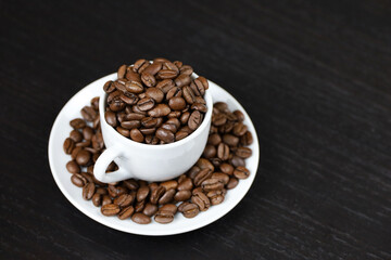Coffee beans in white cup on dark wooden table. Dark and roasted coffee, concept of natural drink