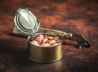 Canned octopus open on a dark blue table with a old can opener. Ready for eat. 