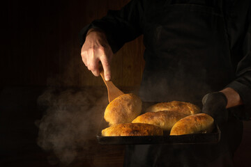 Oven baked buns on a hot baking sheet in the chef hand in glove. The cook takes a hot bun with a...