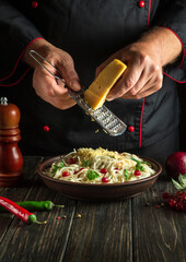 Chef adds hard cheese to spaghetti with spices in a plate. Menu or recipe for a delicious lunch for a hotel or restaurant. Copy space