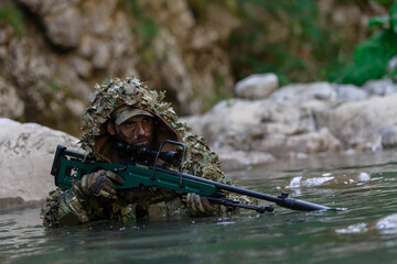 A military man or airsoft player in a camouflage suit sneaking the river and aims from a sniper...