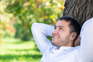 Young man sitting under tree in park on sunny day