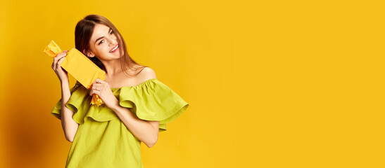 Portrait of young beautiful girl in cute dress posing with present box over yellow background