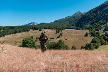 Army soldier holding a sniper rifle with scope and walking in the forest. war, army, technology and...