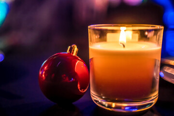 płonąca świeca na wigilijnym stole wraz z czerwoną szklaną bombką