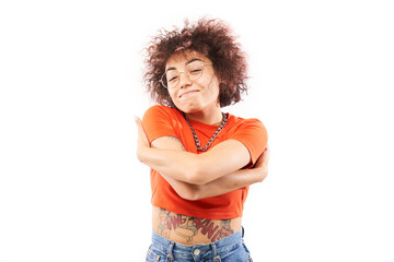 Young curly brunette woman hugging herself and smiling isolated on white studio background. Self...
