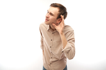 Young brunette man smiling and holding hand near ear, listening carefully, hearing intently...