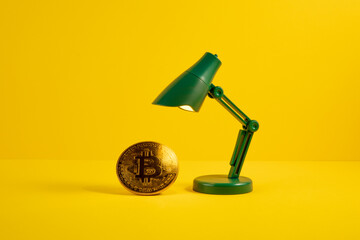 Golden bitcoin iluminated by a green toy lamp on yellow background