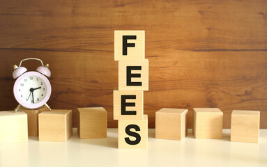 Four wooden cubes stacked vertically on a brown background form the word FEES.