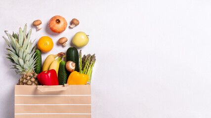 Fresh fruit and vegetables in paper bag on light gray background, top view, copy space
