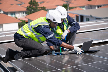 Caucasian and African American engineer man use electric screwdriver and computer notebook working with solar panel on roof factory	
