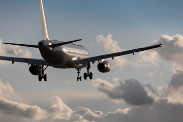 close-up of a silver aircraft in final approach at Stuttgart Airport, against bright cloudy sky. Reflection of the sun in the aircraft, landing gear down