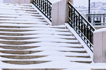 The steps of the granite stairs are covered with snow during a snowfall. Descent to the river on the city embankment.