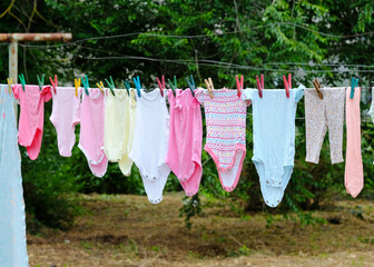Children's things hang on a rope in the courtyard of the house. Clothes for the baby are dried on the street on clothespins. Things of a newborn in different colors from cotton after washing.