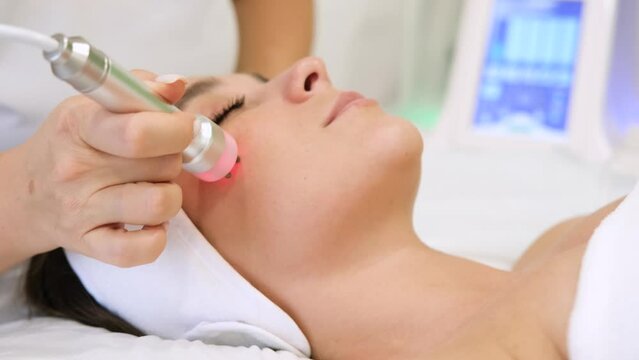 Close-up portrait of a beautiful woman with closed eyes and apparatus for skin rejuvenation. Beauty salon procedures. RF lifting. Microcurrents. Slow motion horizontal video