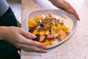 The girl holds a bowl plate with fruit, oatmeal and yogurt with her hands. Healthy eating