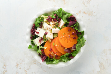 Salad. Fresh green salad with feta cheese, persimmon, pomegranate and pistachio on white plate. Idea for healthy delicious winter Christmas salad. Healthy balanced eating. Top view.
