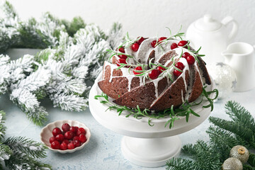 Christmas chocolate bundt cake. Traditional Christmas fruit cake with white glaze, cranberries and rosemary on white stand with Christmas decoration. Winter baking at Xmas or New Year. Copy space.