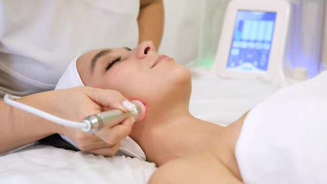 Close-up portrait of a beautiful woman with closed eyes and apparatus for skin rejuvenation. Beauty salon procedures. RF lifting. Microcurrents. Slow motion horizontal video